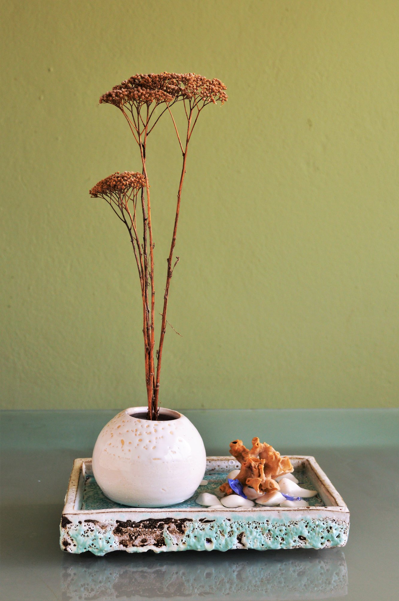 dried flowers in a white round ceramic bowl placed inside a green rectangle ceramic bowl